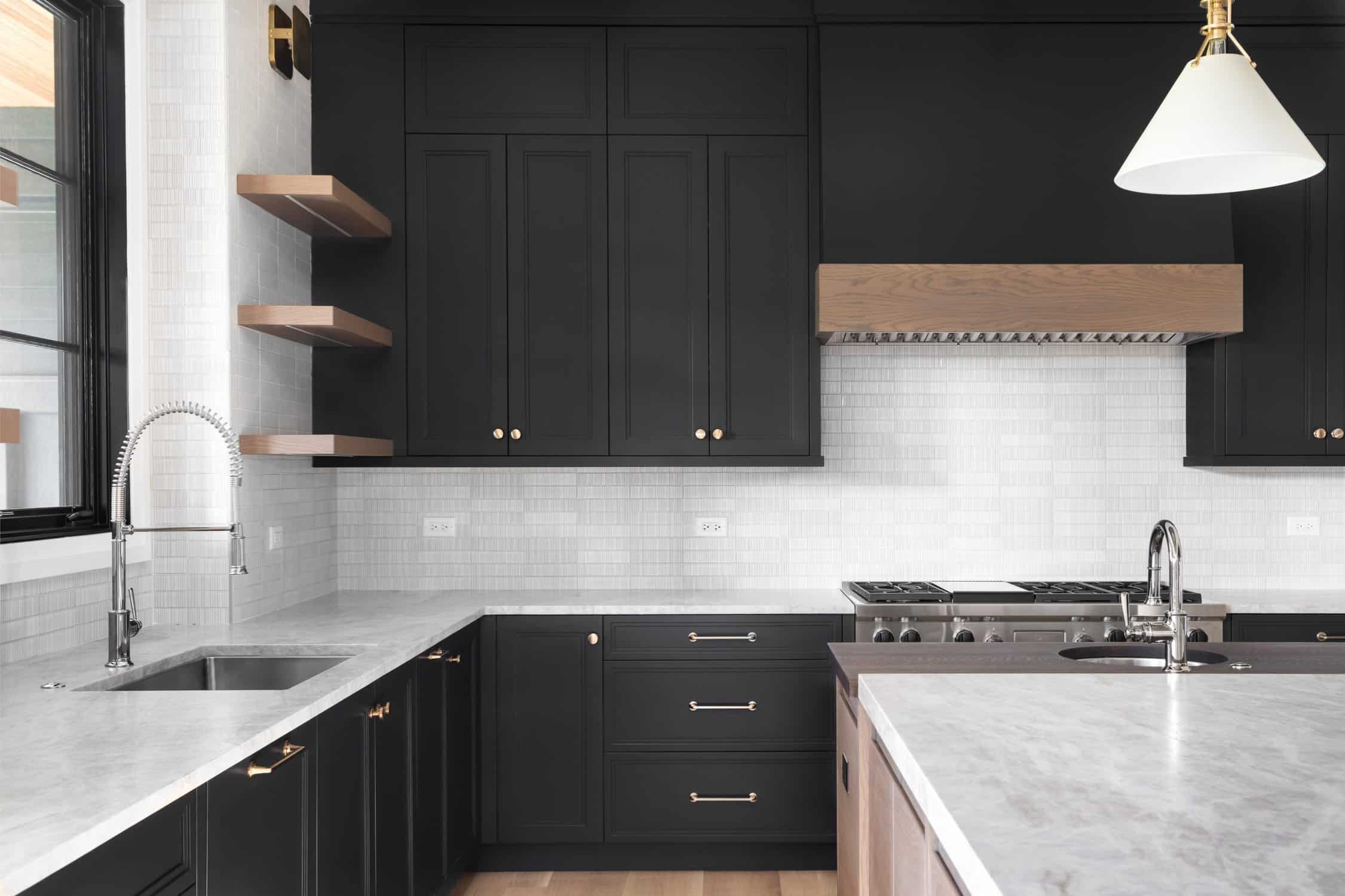 A luxury kitchen with black cabinets, granite counter top, tiled backsplash, stainless steel appliances, and chrome faucets. latest color palettes for interiors