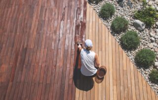 Wood deck renovation treatment, the person applying protective wood stain with a brush, overhead view of ipe hardwood decking restoration process