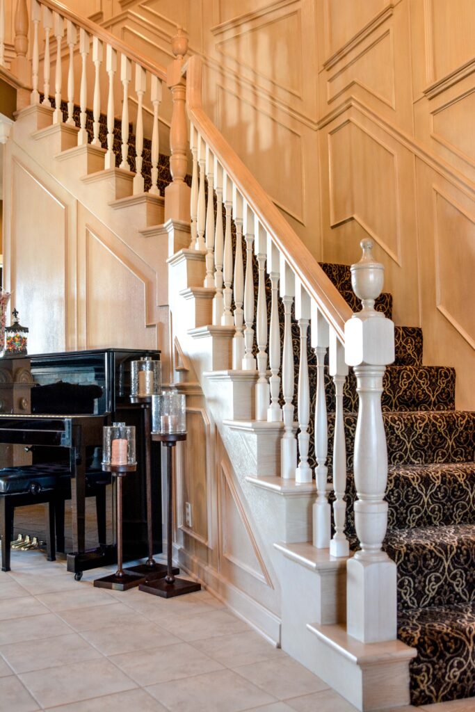 A classic black upright piano sits in front of a curved wooden staircase with a wrought iron railing.